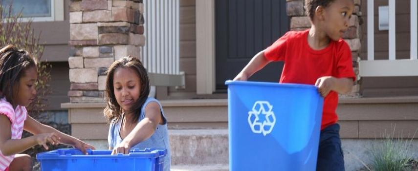 Three children are holding recycle bins and sorting their recyclable materials, outside of their house.